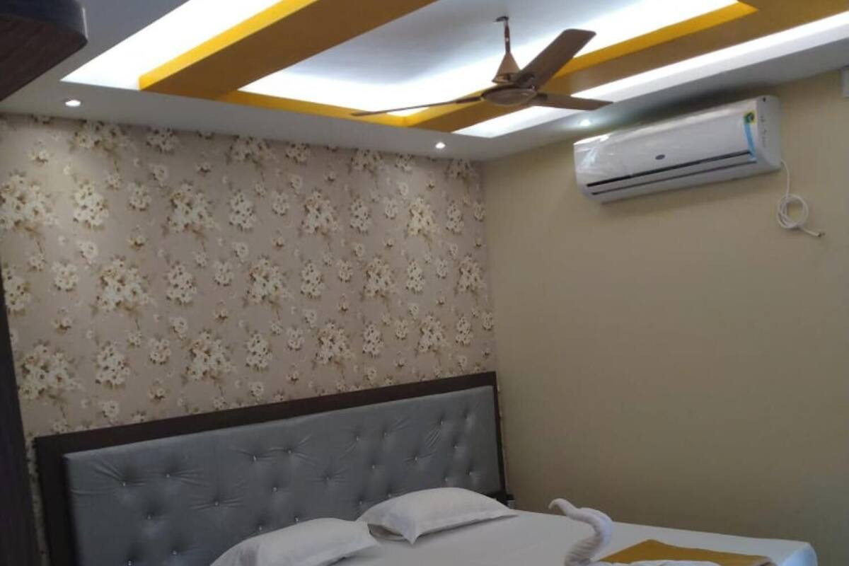 A hotel room with a bed, a desk, a ceiling fan, and an air conditioning unit.