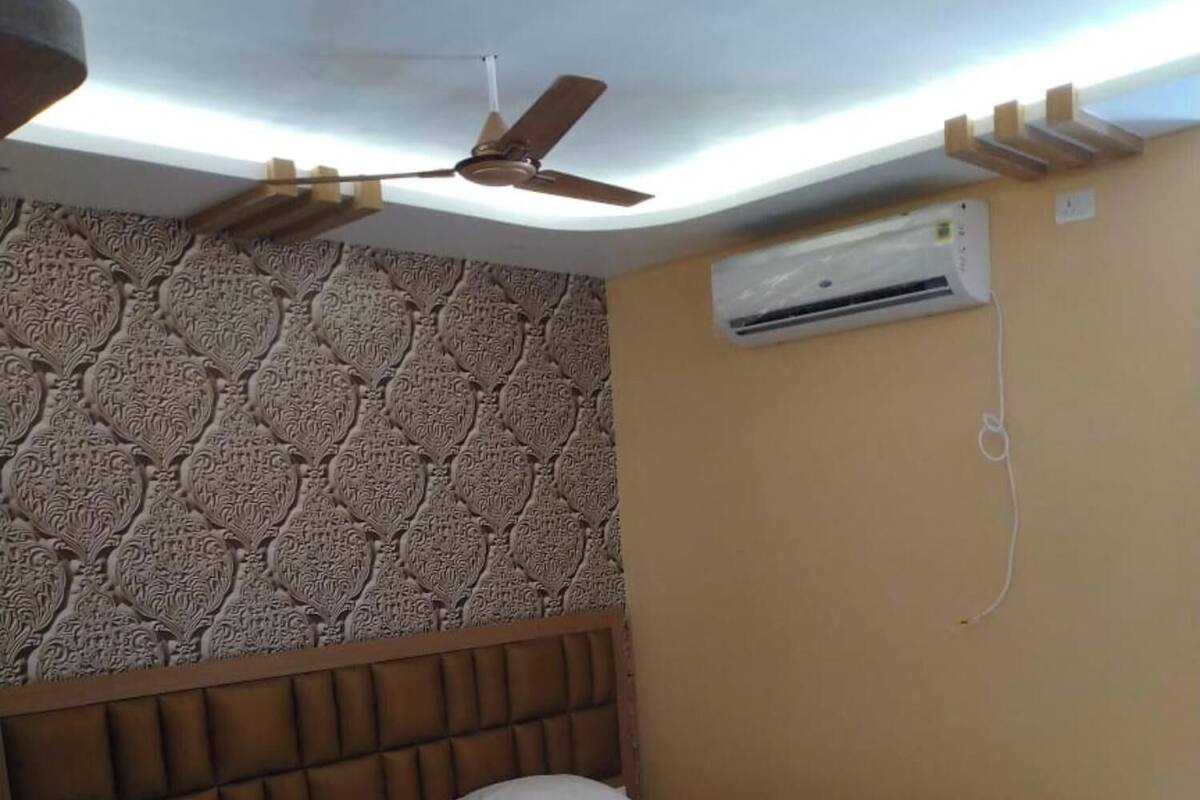 A hotel room with a bed, a ceiling fan, an air conditioning unit, a patterned wall, and a small table.