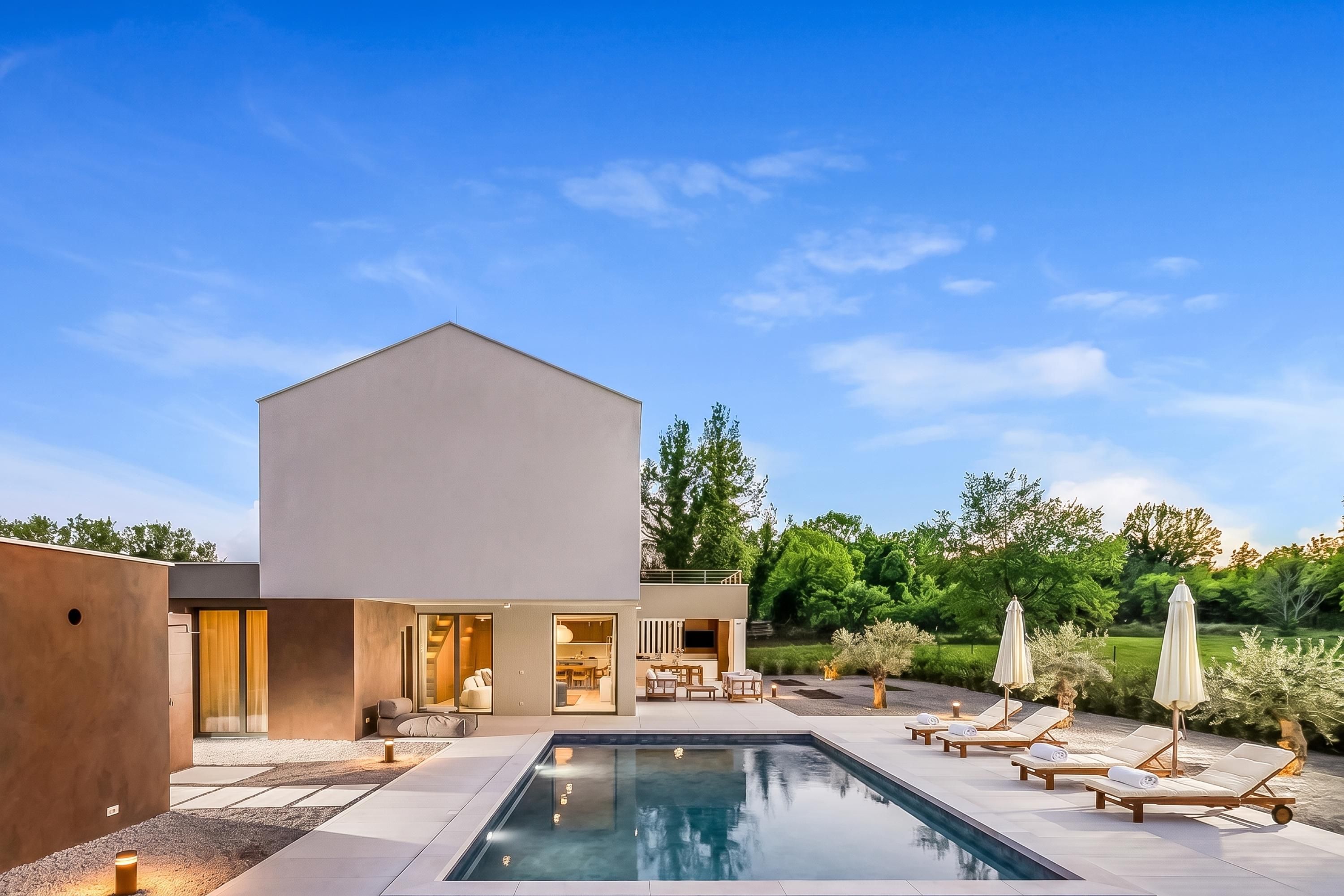 A modern house with a swimming pool, outdoor seating, and a view of the surrounding greenery.