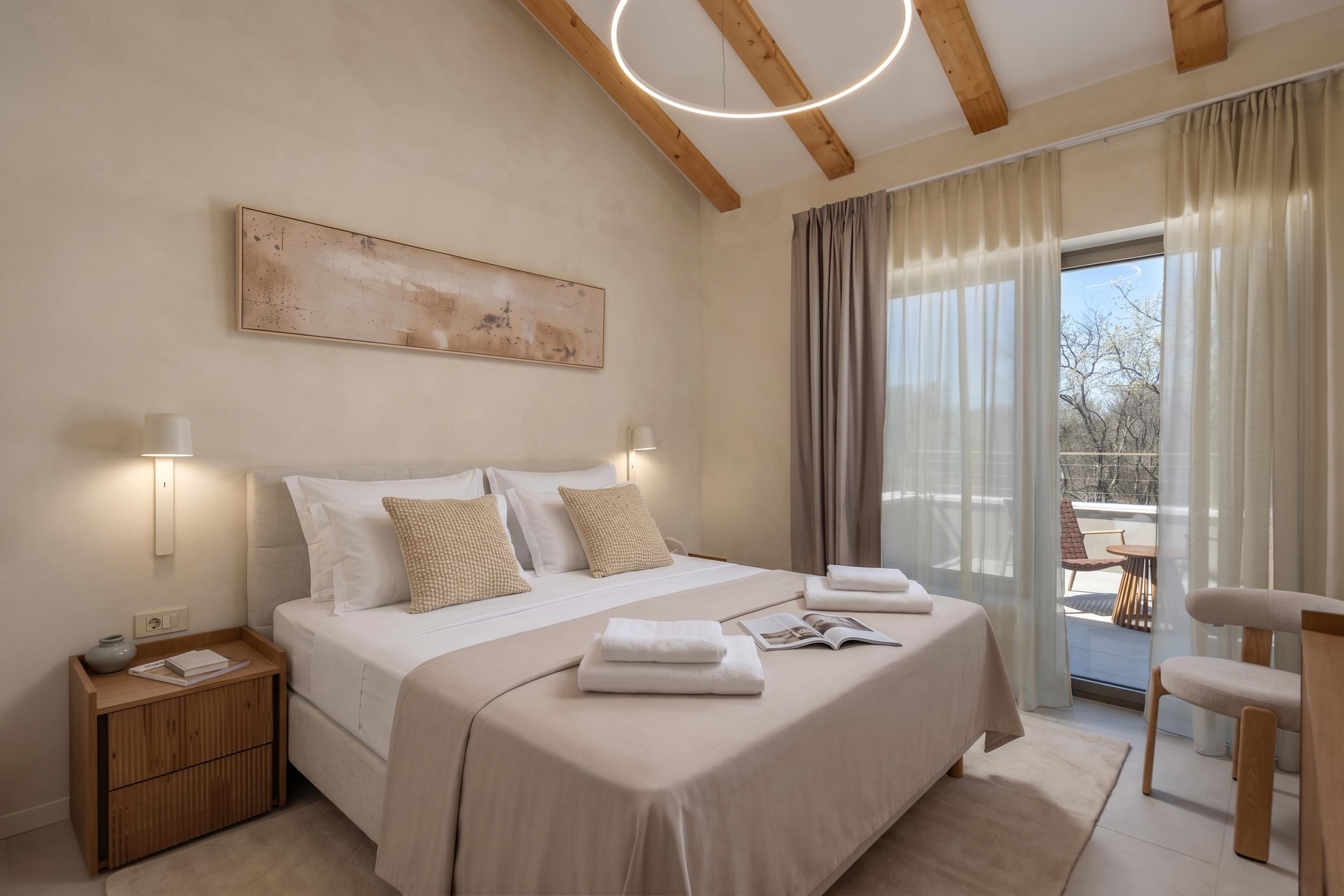 A modern bedroom with a large bed, bedside tables, a view of the outdoors, and a ceiling light fixture.