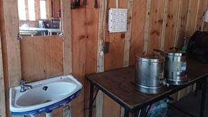 Un interior rústico de madera con un lavabo, espejo, enchufe eléctrico y contenedores metálicos sobre una mesa.
