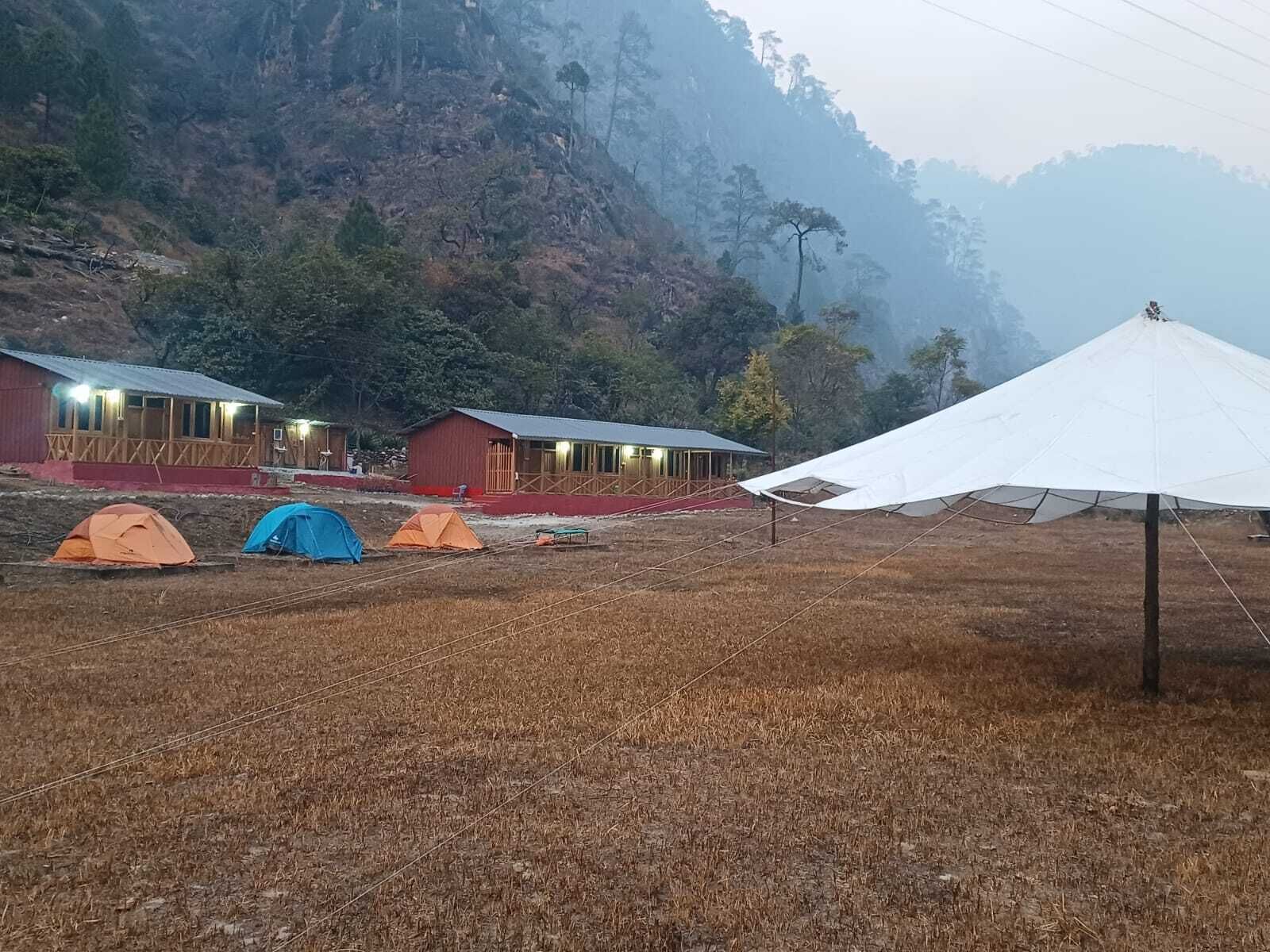 Een camping met tenten en accommodaties, omgeven door droog gras en een bergachtig landschap.