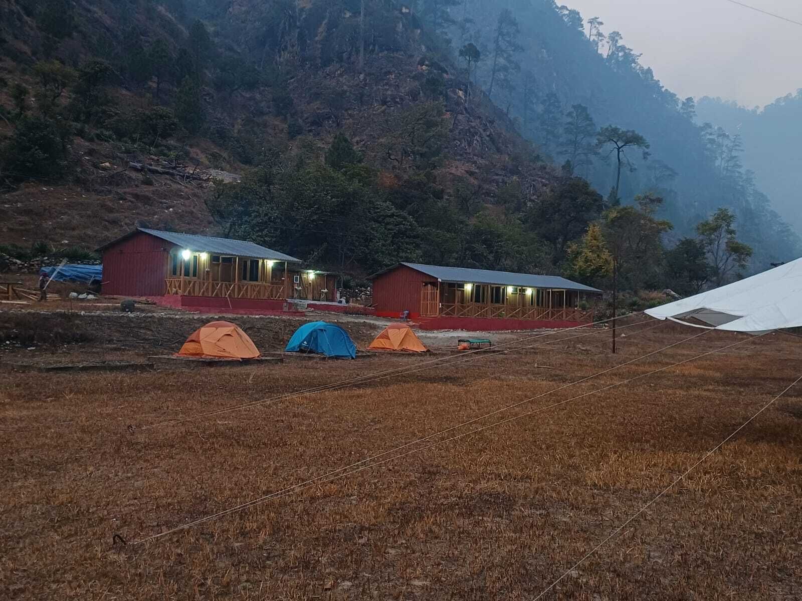 A rural setting with two red buildings, possibly cabins or lodges, and several tents.