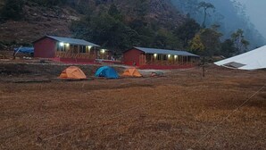 Un entorno rural con dos edificios rojos, posiblemente cabañas o alojamientos, y varias tiendas de campaña.