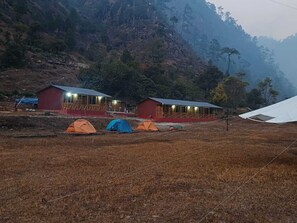 Paisagem rural com duas construções vermelhas, possivelmente cabanas ou alojamentos, e várias tendas.