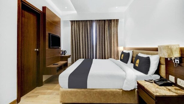 Una habitación de hotel con cama, mesita de noche, lámpara y televisor sobre un mueble.