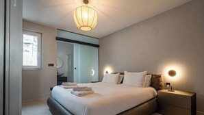 Ein modernes Schlafzimmer mit einem großen Bett, Nachttischlampen und Blick ins Badezimmer.