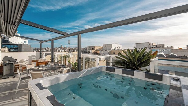 Eine Dachterrasse mit Whirlpool, Sitzgelegenheiten im Freien und Blick auf die Stadt.
