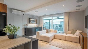 Ein modernes Wohnzimmer mit einer Eckcouch, einem Essbereich und Blick auf die Stadt durch große Fenster.