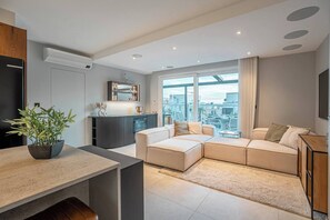 Ein modernes Wohnzimmer mit einer Eckcouch, einem Essbereich und Blick auf die Stadt durch große Fenster.