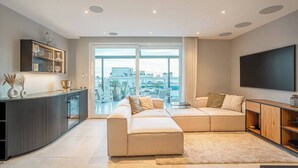 Ein modernes Wohnzimmer mit einem Ecksofa, einem Flachbildfernseher und einem großen Fenster mit Blick auf die Stadt.