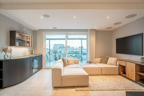 Een moderne woonkamer met een hoekbank, een flatscreen televisie en een groot raam met uitzicht op de stad.