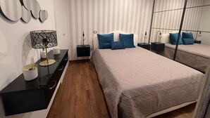 A modern bedroom with a large bed, a nightstand, a lamp, a mirror, and a wall with striped wallpaper. - POMPEII UPSIDE DOWN PENTHOUSE (Scafati)