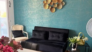 A modern living room with a teal patterned wall, a black sofa, a white chair, a marble coffee table, and a small side table with a plant. - POMPEII UPSIDE DOWN PENTHOUSE (Scafati)