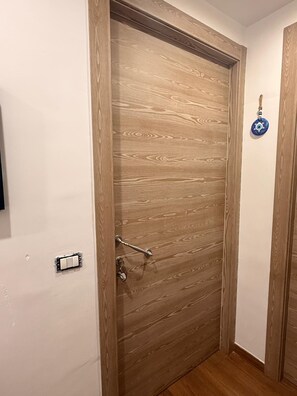 Eine Holztür mit Schlüsselloch und Schloss, eine kleine Wandleuchte sowie eine Steckdose an der Wand.
