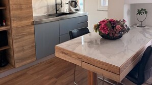 A modern kitchen with wooden cabinets, a marble countertop, a black pendant light, and a vase with flowers on the table. - POMPEII UPSIDE DOWN PENTHOUSE (Scafati)