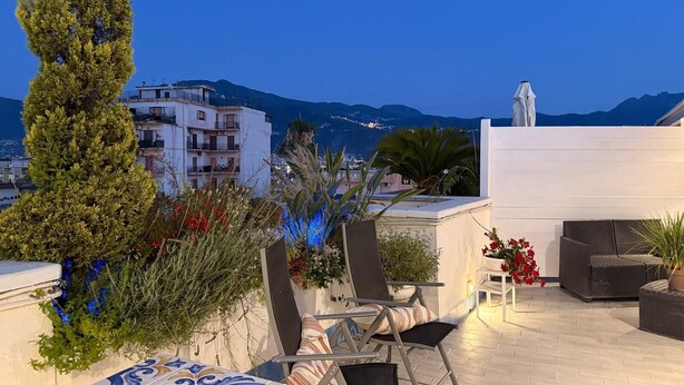A rooftop terrace with a view of a cityscape and mountains, featuring outdoor furniture and potted plants. - POMPEII UPSIDE DOWN PENTHOUSE (Scafati)