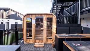 En træsauna med dør, træbænk og et spabad på en træterrasse.