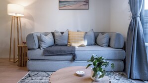 En moderne stue med en grå sofa, et træbord, en gulvlampe og et billede på væggen.