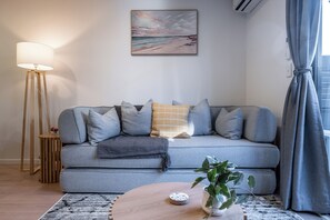A modern living room with a grey sofa, a wooden coffee table, a floor lamp, and a painting on the wall. - Sauna & Spa Escape | Walk to Stadium | CBD (Christchurch)