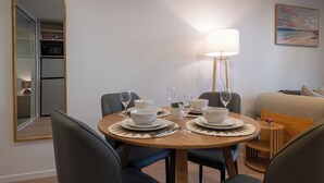 En spiseplads med et rundt bord dækket til fire personer, et spejl, en lampe og et billede på væggen.