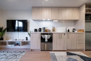 A modern kitchen with built-in appliances, a flat-screen TV, and a dining area with a rug. - Sauna & Spa Escape | Walk to Stadium | CBD (Christchurch)