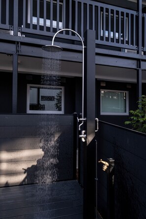A modern outdoor shower with a metal frame, water flowing from a curved spout, and a door with a brass handle. - Sauna & Spa Escape | Walk to Stadium | CBD (Christchurch)