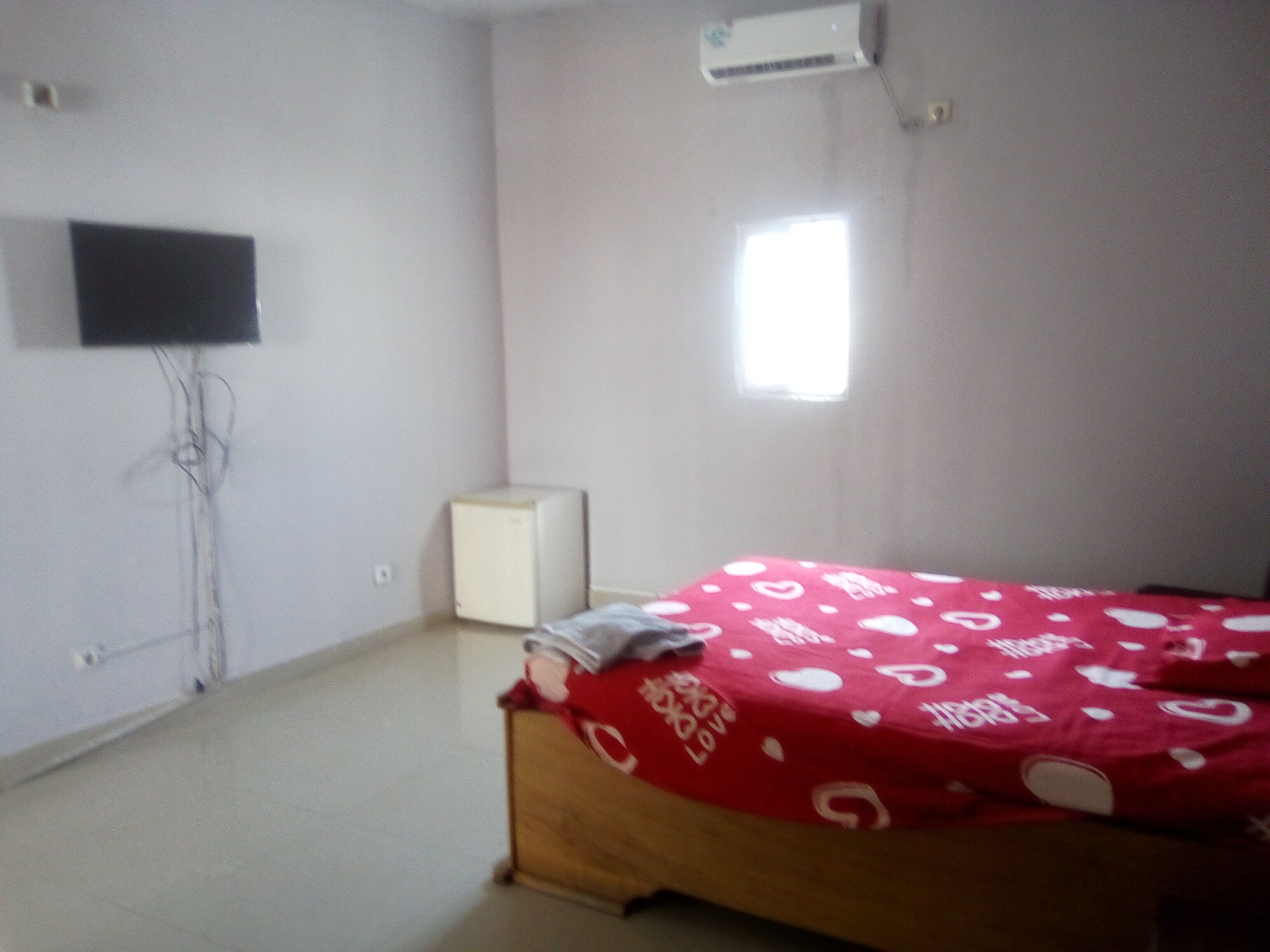 Un dormitorio con cama, televisión, aire acondicionado y ventana.