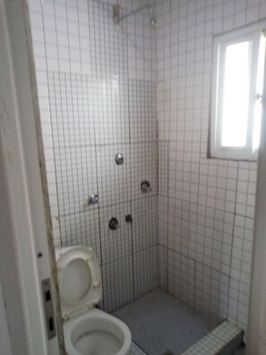 Um banheiro pequeno com azulejos, vaso sanitário, chuveiro e janela.