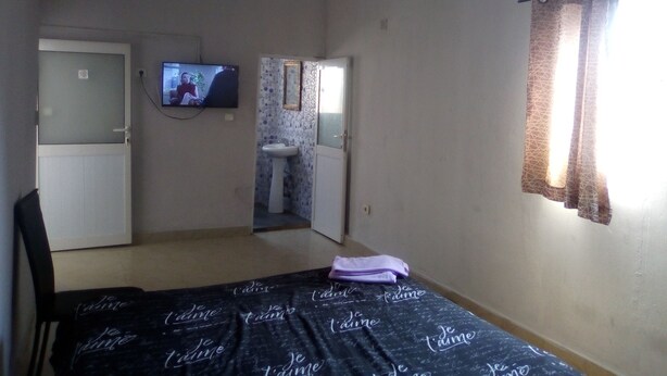 Una habitación con cama, televisión, una puerta y un baño visible a través de otra puerta.