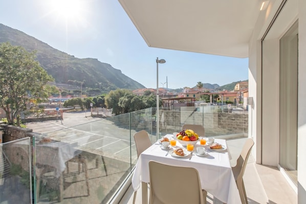 A balcony with a table set for breakfast, a clear view of the surrounding area, and a mountain in the background.