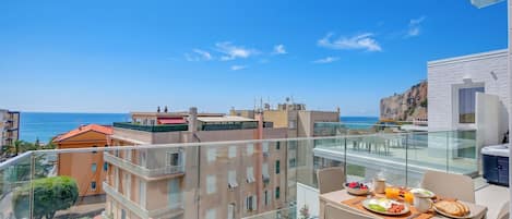 A balcony with a breakfast setup overlooking a coastal cityscape.