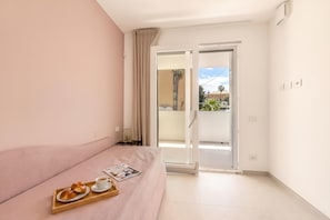 Una habitación con una cama, una bandeja con pasteles y una taza, una revista y un ventanal corredero que da a un espacio exterior.