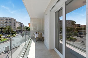 Un balcone con tavolo e sedie, ringhiera in vetro e vista sulla strada e sugli edifici.