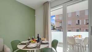 Zona de menjador amb una taula preparada per a dues persones, un sofà verd i una vista d'un edifici a través d'una porta de vidre.