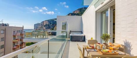 A balcony with a dining setup, a hot tub, and a view of the sea and buildings.