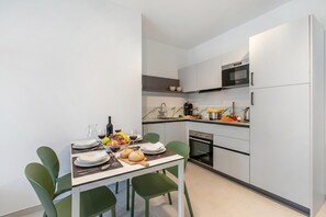 Una cocina moderna con armarios blancos, horno empotrado y comedor con sillas verdes y una mesa preparada para una comida.