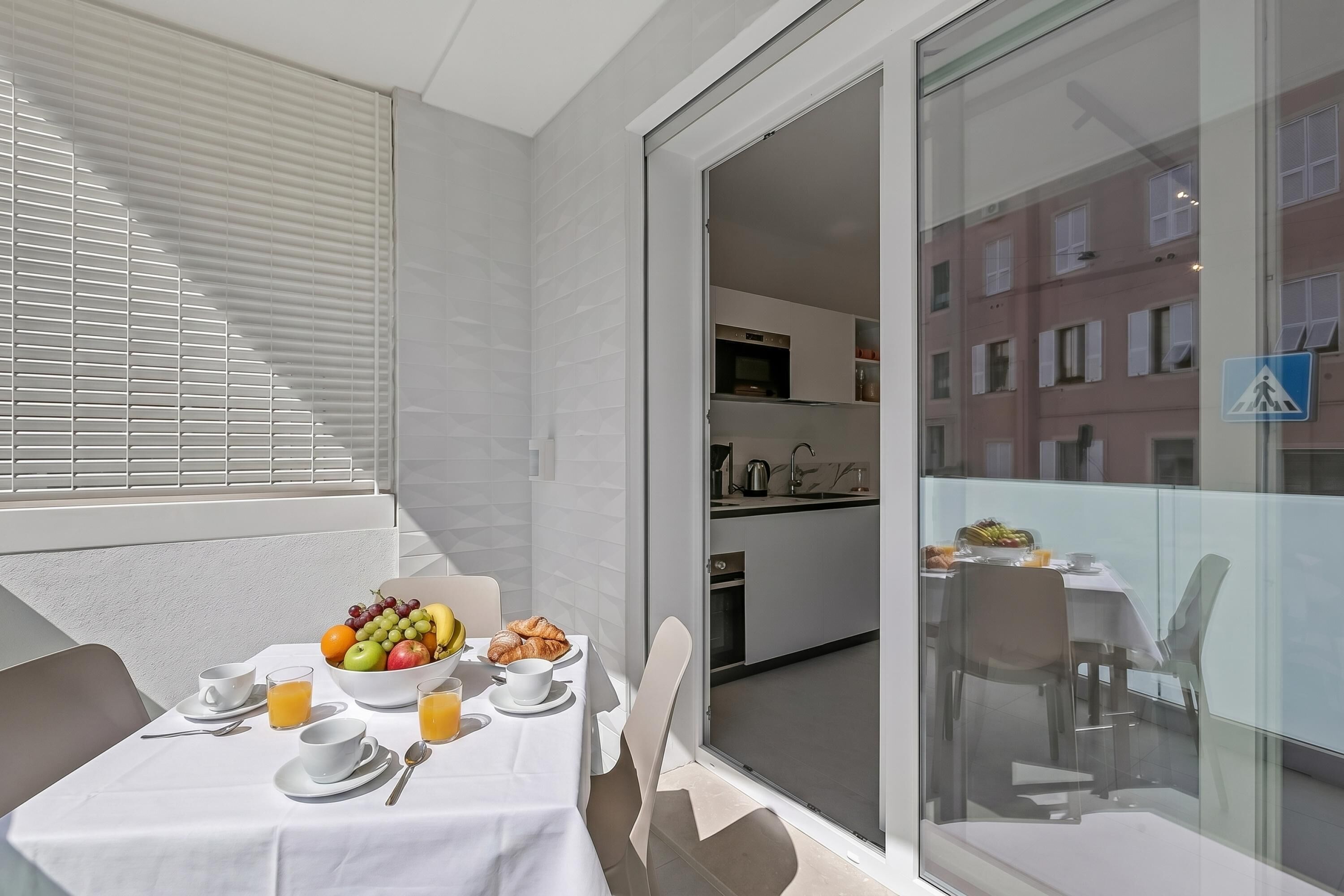 En balkon med et bord dækket til morgenmad, en skål med frugt og en croissant.