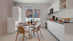 Una cuina moderna amb armaris blancs, una zona de menjador amb una taula rodona i cadires, i una vista a l'exterior a través d'una porta de vidre.