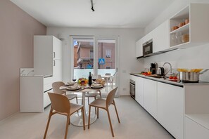 A modern kitchen with white cabinetry, a dining area with a round table and chairs, and a view through a glass door to the outside. - Nua Boutique Apartaments (Finale Ligure)