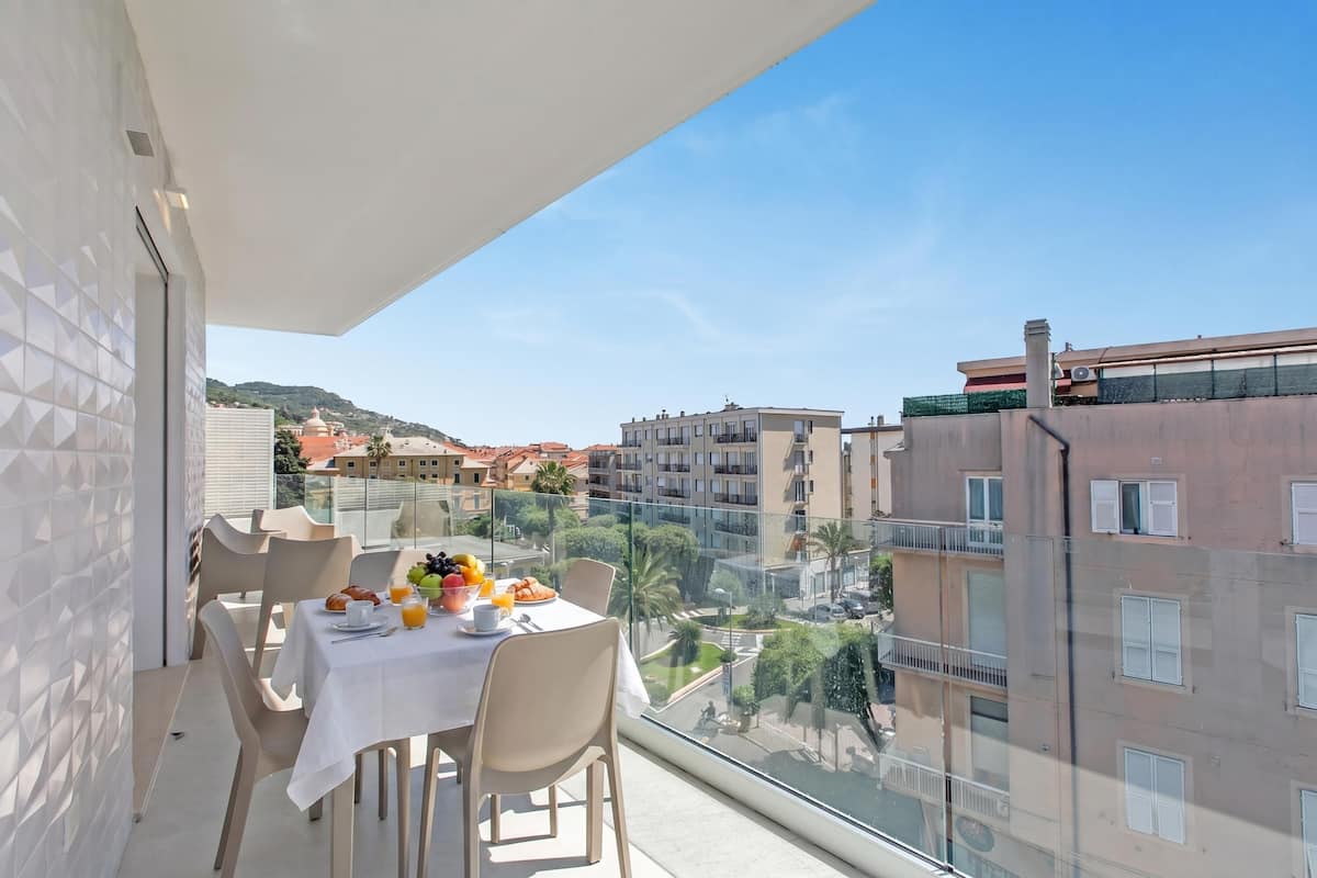 A balcony with a table set for breakfast, overlooking a cityscape with buildings and greenery.