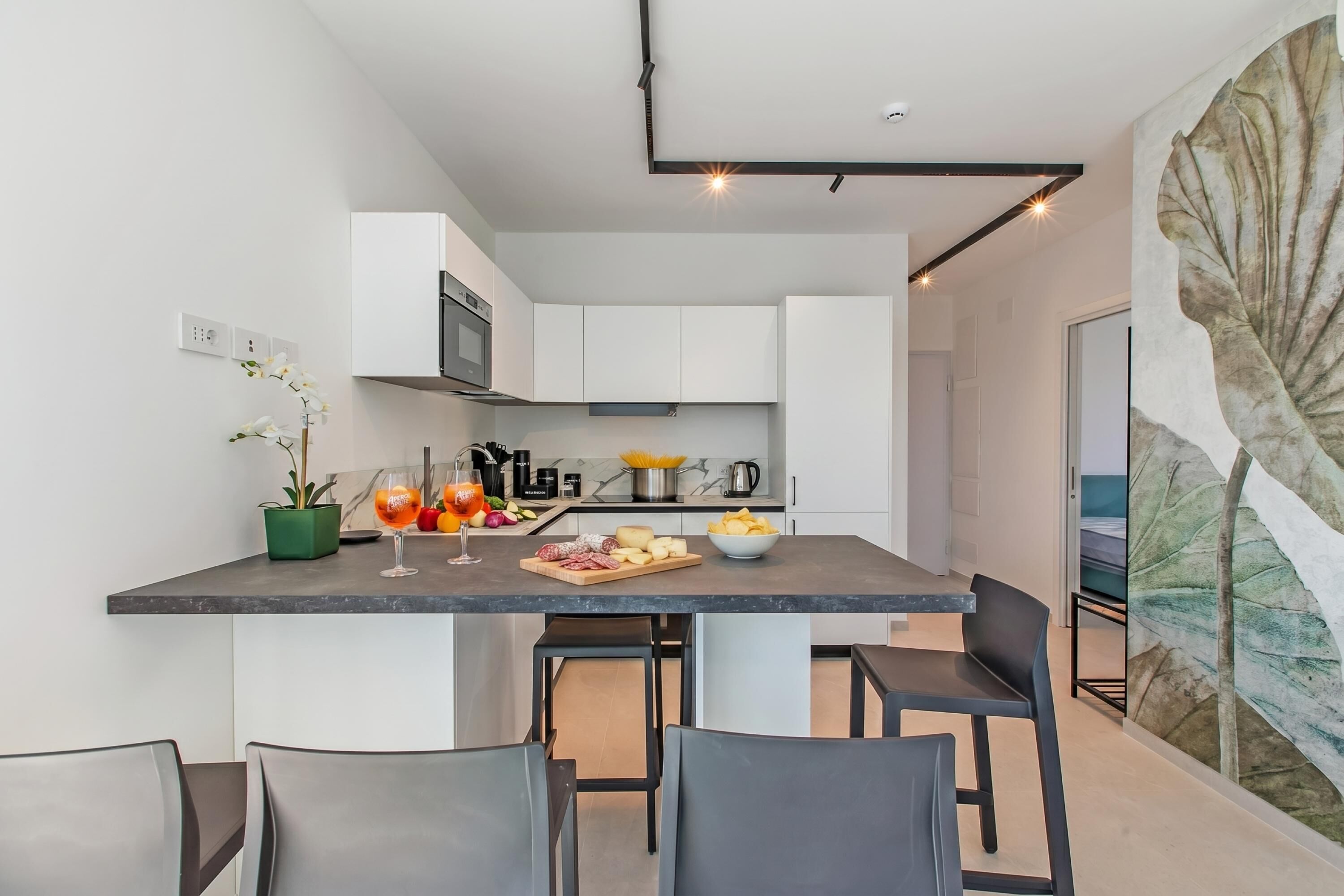 A modern kitchen with white cabinets, a marble countertop, and a dining area with black chairs.