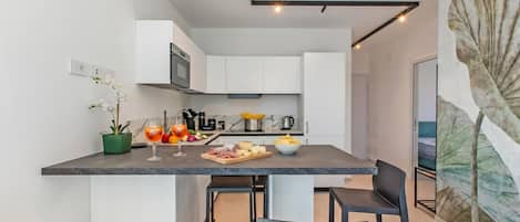 A modern kitchen with white cabinets, a marble countertop, and a dining area with black chairs.