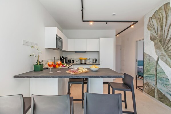 A modern kitchen with white cabinets, a marble countertop, and a dining area with black chairs.