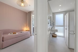 Ein modernes Hotelzimmer mit einem rosafarbenen Sofa, einem Nachttisch mit Lampe und einem großen Fenster.