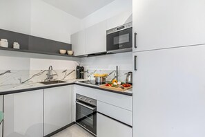A modern kitchen with white cabinets, a marble backsplash, stainless steel appliances, and a wooden cutting board with vegetables. - Nua Boutique Apartaments (Finale Ligure)