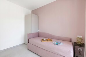 A minimalist room with a pink sofa, a small table with a cup and a pastry, a magazine, and a decorative lamp on a nightstand.