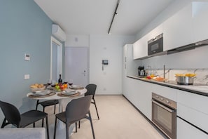 Una cocina moderna con armarios blancos, horno empotrado y comedor con mesa lista para dos.