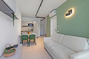 A modern living room with a white sofa, a dining area with a table and chairs, and a kitchen in the background.