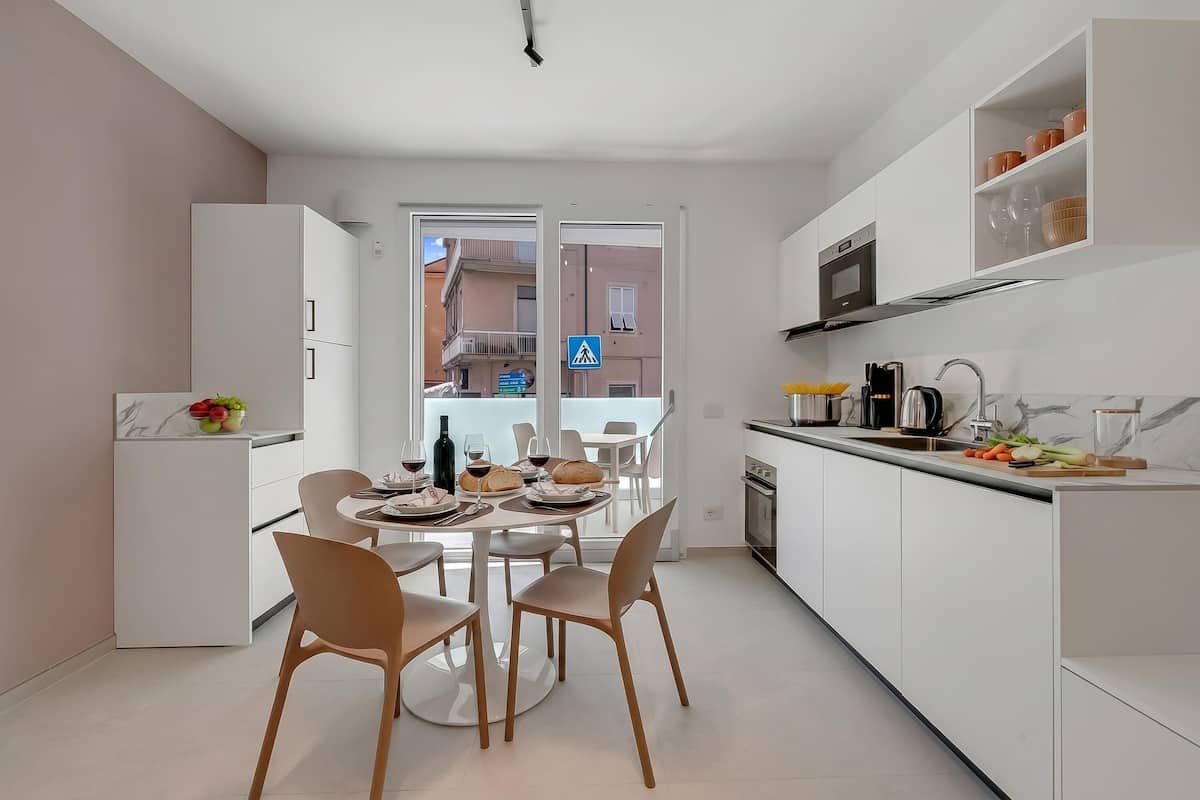 A modern kitchen with white cabinets, a dining table with chairs, and a view of the outside.